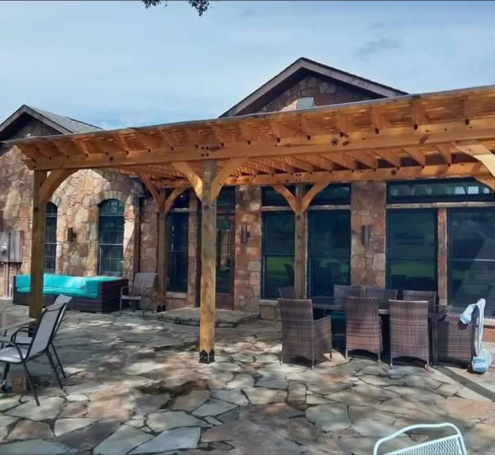 Attached cedar pergola over a flagstone patio on a stone home built by Forged Fence & Deck in Pearland, TX
